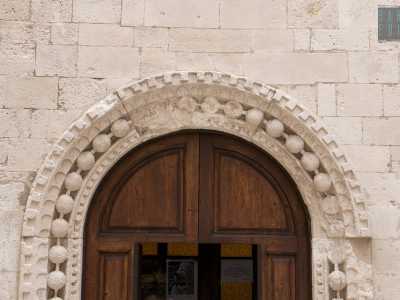 Il piccolo portale in legno � inserito in una perimetro decorativo di spessi grani di rosario in pietra, incastonato in una doppia cornice dentellata